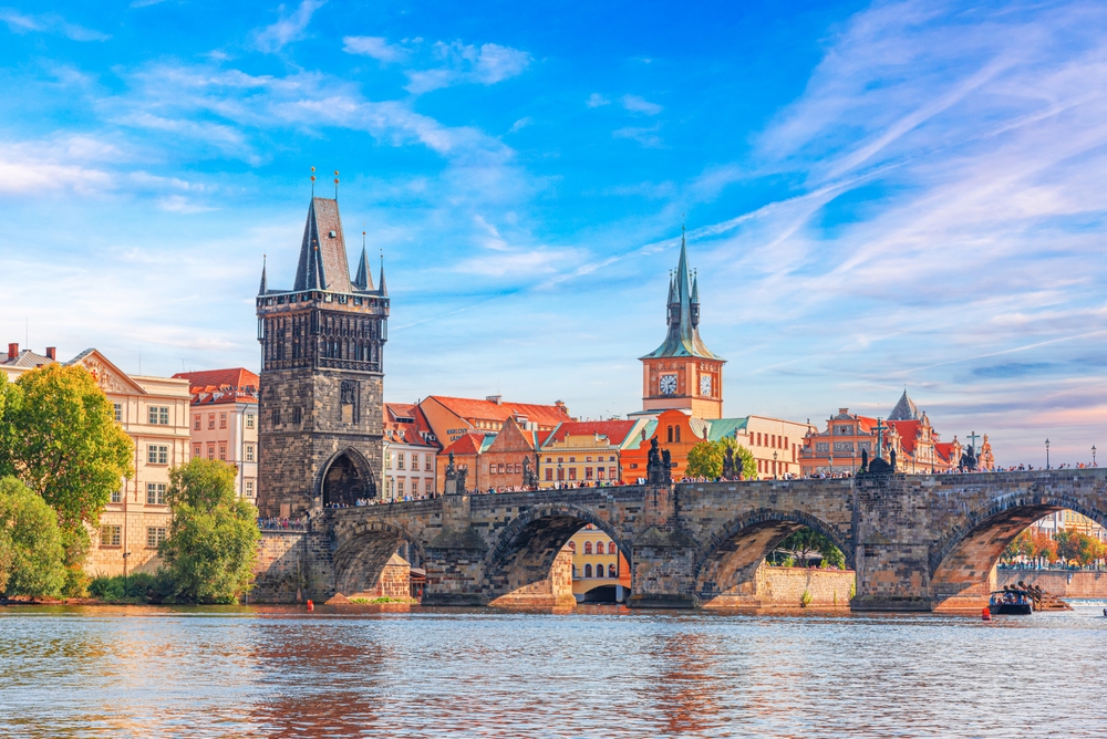 Scenic aerial view of Charles Bridge at sunset in Prague, Czech Republic, with the Vltava River and historic Old Town skyline.